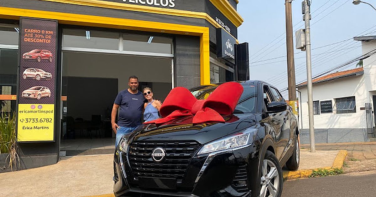 Casal recebendo um carro 0km com laço vermelho em frente à loja Érica Martins Veículos, em São Paulo
